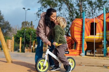 Mom teaches her little son to ride a bike without pedals. A boy on a balance bicycle. Along with the boy is the mother and supports the bike.