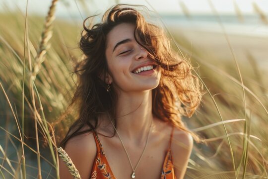 Joyful young woman smiling in a sunny field of tall grass, with a soft-focus beach background.