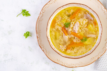 Fresh chicken soup with vegetables and stelline pasta in a bowl with carrot and parsley. Top view, flat lay