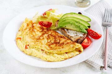 Omelette with tomatoes and toast with avocado on white plate.  Frittata - italian omelet.