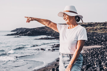 Happy carefree senior woman with white hat looking at new day from sea beach at sunrise enjoying...