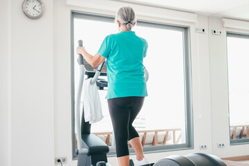 Back view of active senior woman excercising on stepper at gym to stay fit. Cardio excercises for mature people. Athleticspirit concept