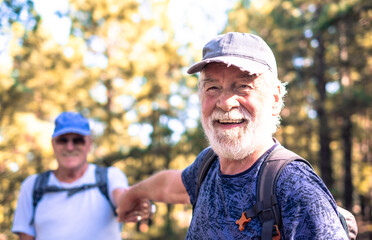 Happy smiling couple of elderly men with hat and backpack look in camera while enjoying mountain...