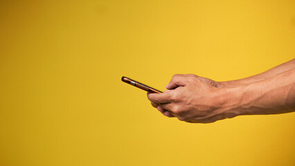 The man's hand holds the smartphone on yellow background, concept. Touchscreen tablet, copy space.