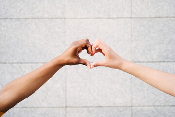 Close up of two multicultural hands join together form heart with background wall. Hope and love between homosexual relationships, human beings of different races with different skin color. Copy space