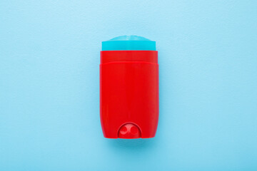Red plastic stick of armpit deodorant on light blue table background. Pastel color. Male daily...