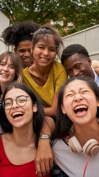 Vertical selfie of young group excited students looking at camera laughing. Happy to be back at school and be together with classmates. Portrait of multirracial teenagers friends enjoying having fun.