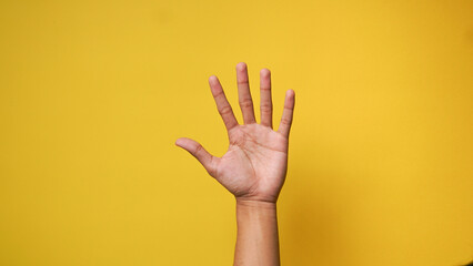 Man's hand lifting up and waving saying hi or asking permission on a yellow background