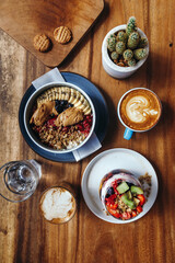 Healthy breakfast with chia strawberry pudding, oatmeal bowl with banana, peanut butter, blackberries, raspberries, nuts, seeds and goji berries and a cup of hot soybeans cappuccino