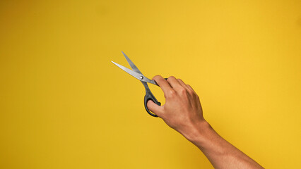 Man's hand holding black scissors on a yellow background