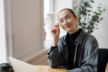 Stylish professional woman working on laptop with a serene expression.