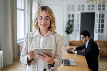 Smiling businesswoman with digital tablet, colleague working in background.