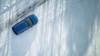 Aerial top down view of a blue car driving on icy and snowy, road during winter, difficult winter...