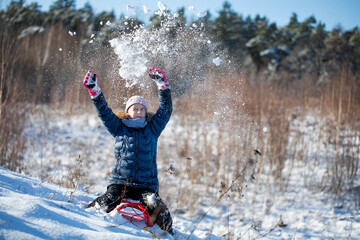 dziewczynka na sankach rzuca śnieżkami, zabawa na śniegu
