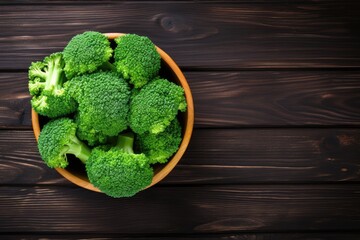 Top-down view of a rustic surface with a text space, displaying a bowl of cooked broccoli sprinkled with sea salt.