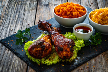 Roasted chicken drumsticks with sauerkraut and grated carrot on stony black plate on wooden table
