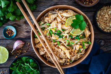 Pad Thai with chicken nuggets and rice noodles in peanut and tamarind sauce on wooden table in eco...