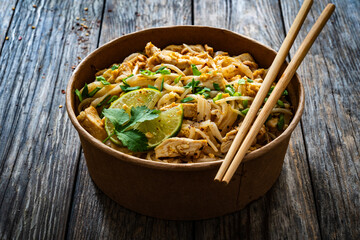 Pad Thai with chicken nuggets and rice noodles in peanut and tamarind sauce on wooden table in eco bowl to go
