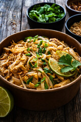 Pad Thai with chicken nuggets and rice noodles in peanut and tamarind sauce on wooden table in eco bowl to go
