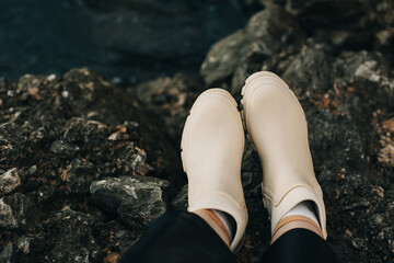 A top down view of a woman standing near the sea wearing rubber boots.
