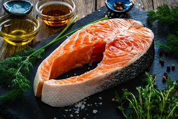 Fresh raw salmon steak with salt and fresh vegetables on wooden background
