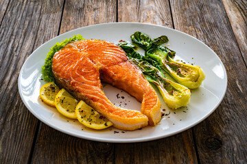 Fried salmon steak with lemon and steamed pak choi cabbage served on wooden table
