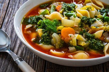 Pistou soup Nice - broth with basil pesto, noodles and vegetables on wooden background in white bowl