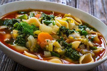 Pistou soup Nice - broth with basil pesto, noodles and vegetables on wooden background in white bowl