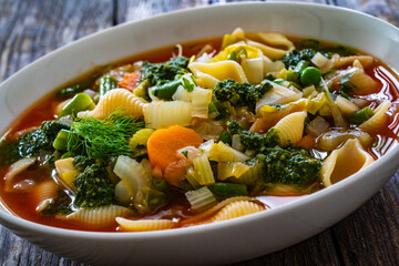 Pistou soup Nice - broth with basil pesto, noodles and vegetables on wooden background in white bowl