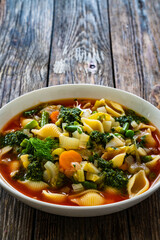 Pistou soup Nice - broth with basil pesto, noodles and vegetables on wooden background in white bowl