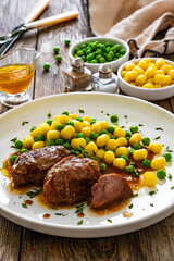 Baked pork cheeks in sauce with gnocchi and green peas on wooden table
