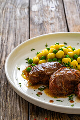 Baked pork cheeks in sauce with gnocchi and green peas on wooden table
