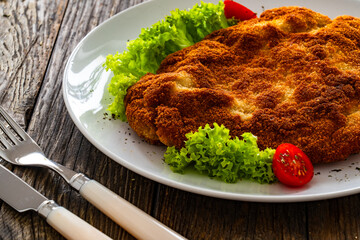 Crispy breaded fried pork chop and fresh vegetables on wooden table
