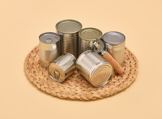 Canned food in metal cans on a wicker mat. Can opener with wooden handle.
