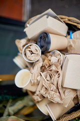 Paper garbage in a basket on the street, disposable tableware in a basket. Disposable paper tableware, cardboard, used cups and plates