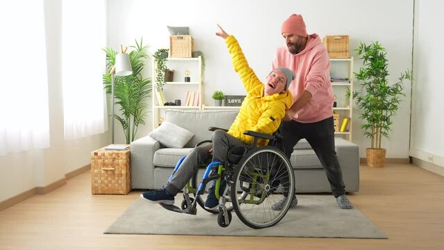 Happy disabled man in wheelchair and friend celebrating raising hands at home
