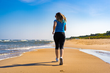 Mid adult beautiful woman running on sunny beach 