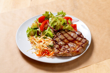 Grilled beef steak with cabbage, lettuce and tomatoes on a white plate.