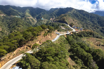 Aerial view of a winding road cutting through a lush mountain landscape with scattered settlements...
