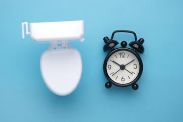 Flatlay picture of toilet bowl and alarm clock. Toilet break concept.