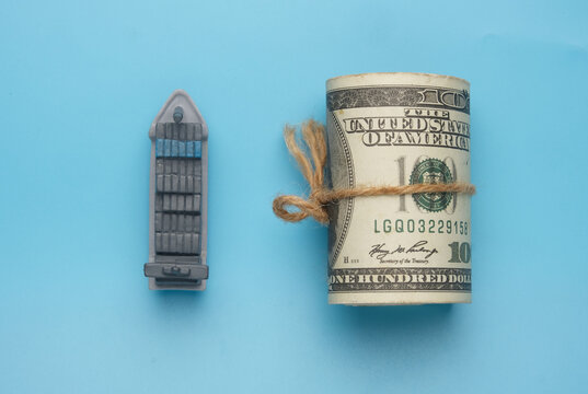 Flatlay picture of vessel miniature with roll fake money on blue background. Shipment cost