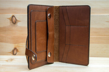 Men's wallet made of rough brown leather on a light wood background. A stylish accessory for men,...