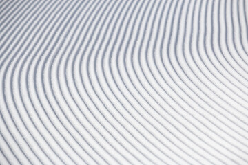 Curve lines in groomed winter snow surface on white ski slope abstract texture background