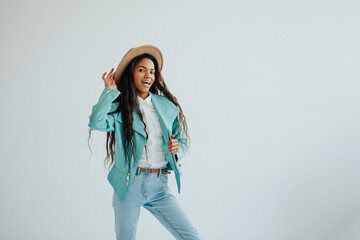 joyful african teenager in a mint jacket and beige hat posing in a spacious bright room. 