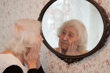 Portrait of old senior woman looking into a mirror at home