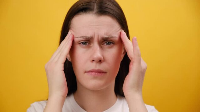 Close up portrait of unhappy young woman rubs temple, closed eyes suffers headache painful feelings chronic migraine hurt, isolated on yellow background. Divorce, difficult period of life concept 