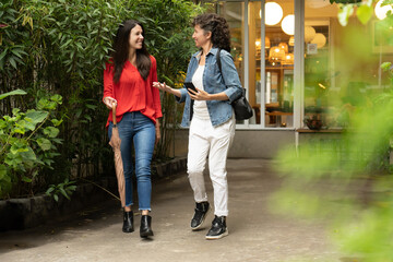 Two female friends walking off a hotel while talking and smiling. Two female friends planning a...
