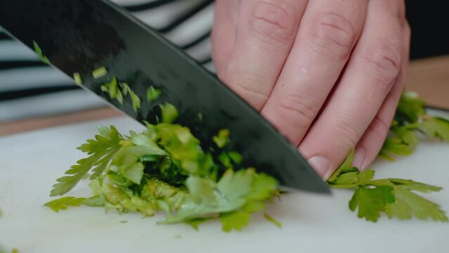 hands finely chopping parsley on white cutting board with a knife. The wooden surface and striped apron provide This image is suitable for stock sites, highlighting culinary skills 