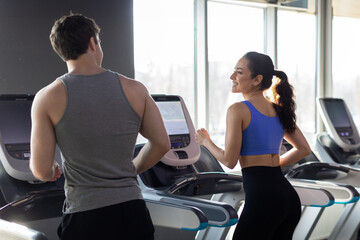 Attractive european young couple running on treadmill at gym, enjoying working out together, looking at each other, talking and smiling, rear view