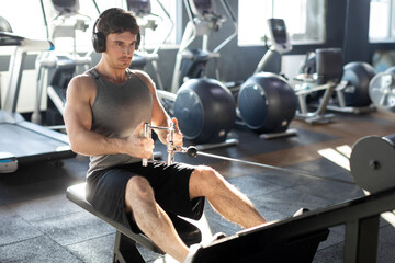 Young muscular man focusing on his cable workout, wearing headphones and listening music, with...
